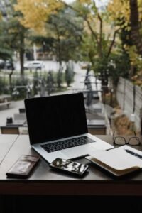 A minimalist workspace with a laptop, notebook, and eyeglasses on a wooden table.
