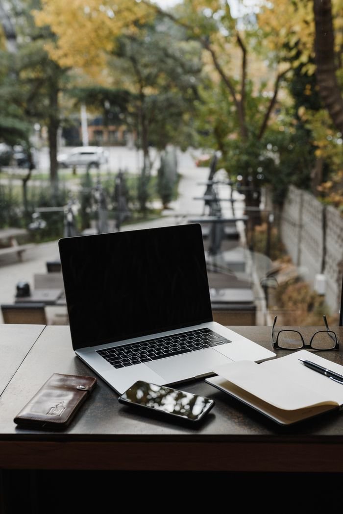 A minimalist workspace with a laptop, notebook, and eyeglasses on a wooden table.